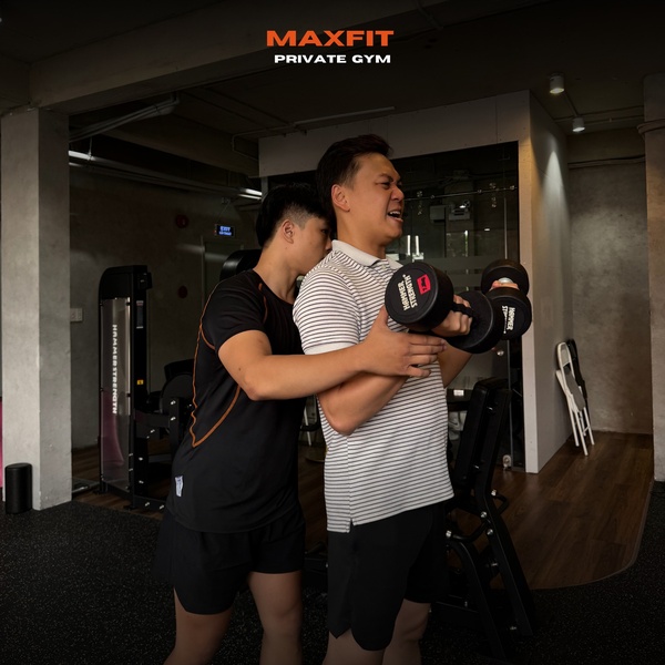 This ad creative shows a personal trainer assisting a client with a dumbbell chest press, emphasizing professional guidance in a private gym setting.
